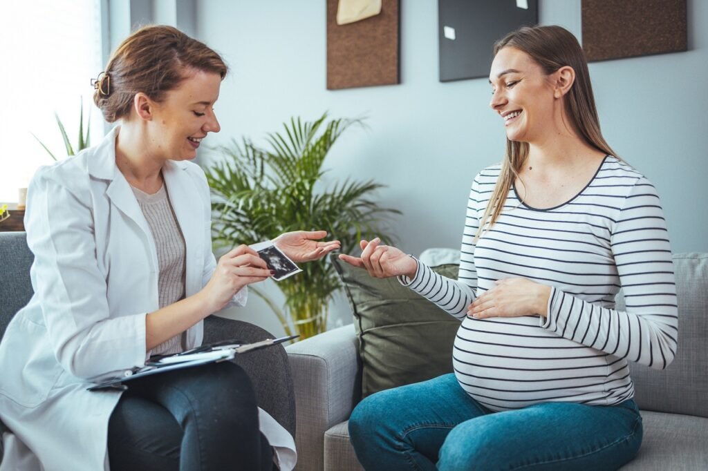 Young woman smiles while looking at her baby's ultrasound image. She is meeting with a home healthcare nurse. Pregnant woman and doctor looking at her baby ultrasound picture